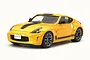 A studio shot of a yellow Tamiya 1/24 scale Nissan 370Z Heritage Edition model car with black racing stripes on a white background.