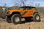 An orange Axial Wraith 1.9 RC rock racer truck parked on a dirt trail in an outdoor desert environment.