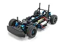 A high-angle studio shot of a Tamiya M-07R 1/10 scale RC touring car chassis kit, featuring black plastic components and blue anodized aluminum parts.