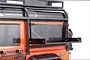A black aluminium drop-down tool bench mounted on the rear side window of an orange RC Land Rover Defender body.