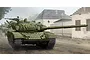 An artistic illustration of a Russian T-72A main battle tank moving down a dusty road past damaged buildings.