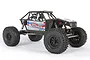 Side profile of an Axial Capra 1.9 Unlimited Trail Truck RC rock crawler, featuring a black tube chassis, driver figures, and large off-road tires.