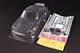 An unpainted clear polycarbonate RC car body shell of a Porsche 911 Carrera RSR, including decal sheets, window masks, and small plastic parts.