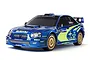 A 1/10 scale Tamiya RC model of the 2004 Subaru Impreza WRC rally car in blue with gold wheels and official rally team decals.