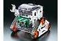 Tamiya Microcomputer Crawler Robot kit featuring white frame, orange wheels, black tracks, and an ultrasonic sensor module on a black background.