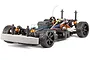 A studio shot of an HPI Sprint 2 RC car chassis without a body shell, featuring black wheels, orange shock absorbers, and a foam front bumper.