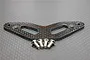 A GPM Racing graphite upper bumper plate with four included metal screws, displayed on a textured grey surface.