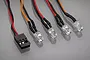 A set of four clear LED lights wired together with a black connector plug on a grey reflective surface.