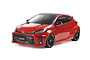 A studio shot of a Tamiya 1/10 scale Toyota GR Yaris RC car model in red with black wheels on a white background.