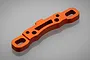 An orange anodized aluminium suspension arm pin mount for an RC car, shown from an angled top-down perspective on a grey background.