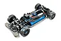 A high-angle studio shot of a Tamiya TT-02R 1/10 scale RC touring car chassis, showing the black plastic frame, blue battery, and electric motor.