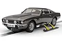 A 1/32 scale Scalextric James Bond Aston Martin V8 slot car in dark grey, featuring deployed side skis, positioned on a slot car track against a white background.