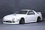 A white Mazda RX-7 FC3S RC drift car body shell, painted and mounted on a chassis with bronze wheels, set against a dark grey background.
