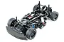 A high-angle studio shot of a Tamiya M-07 Concept 1/10 scale RC touring car chassis, showing the black plastic frame, suspension, and rubber tires.