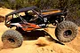 An Axial Wraith RC rock racer driving over a dirt mound in an outdoor setting.