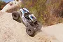 An Axial Yeti RC rock racer driving up a sandy hill, kicking up dust in an outdoor setting.