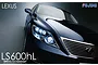 A close-up studio shot of a dark blue Lexus LS600hL model car, showing the front headlight, grille, and Lexus emblem against a dark gradient background.