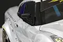 A close-up view of a black racing-style side mirror mounted on a white RC drift car body.