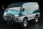 A 1/10 scale RC rock crawler van model, painted metallic teal and silver, featuring a bull bar with auxiliary lights, set against a black background.