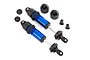 Two blue anodized aluminum Traxxas GT-Maxx RC shock absorbers without springs, shown with included plastic mounting hardware and pistons on a white background.