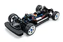 A high-angle studio shot of a Tamiya TT-02SRX 1/10 scale RC touring car chassis, showing the black plastic frame, white wheels, and blue anodized components.
