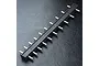A black MST pinion caddy tool with multiple metal pegs for organizing RC pinion gears, set against a textured black background.