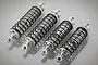 Four Rovan silver aluminium adjustable RC shock absorbers arranged in a row on a reflective grey surface.