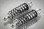 Two silver aluminium adjustable RC shock absorbers with black springs on a reflective grey background.