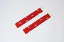Two strips of red double-sided adhesive tape with 3M branding on the backing, laid diagonally on a white background.