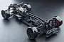 A high-angle studio shot of the MST MRX S 1/10 scale RWD RC drift car chassis, featuring a black frame, electric motor, and drift tires on a textured surface.