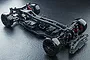 A high-angle studio shot of an assembled MST RMX 2.5 S+ RC drift car chassis, featuring black plastic components, red accents, and smooth drift tires.