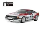 A studio shot of a Tamiya TT-02 Toyota GT-Four ST165 RC rally car with a white and red pre-painted body, featuring racing decals and white O.Z. Racing wheels.