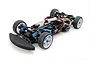 A high-angle studio shot of a Tamiya TA08R 1/10 scale RC touring car chassis, featuring blue anodized aluminum parts, carbon fiber components, and white wheels.