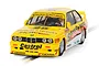 A 1/32 scale Scalextric BMW E30 M3 slot car in yellow Benson & Hedges racing livery on a track.