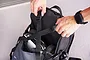 A person adjusting the straps on a black Koswork RC expandable backpack, with an RC car visible inside the main compartment.