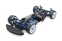 High-angle studio shot of a Tamiya TRF421 1/10 scale RC touring car chassis, featuring blue anodized aluminum parts, carbon fiber deck, and white wheels.