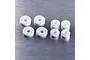 A set of eight white plastic RC shock pistons and spacers arranged on a brushed metal surface.