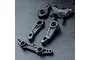 A set of black plastic RC steering assembly components including steering arms and a bridge piece on a textured black surface.