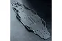 A black plastic MST RC car chassis plate featuring molded structural ribs and mounting holes, viewed from a high angle against a dark textured background.