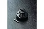 A black aluminium spur gear mount for an RC car, shown with a small metal pin on a textured black surface.
