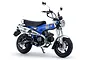 A studio shot of a 1/12 scale Tamiya Honda Dax125 motorcycle model kit, featuring a metallic blue frame, silver exhaust, and black seat.