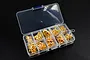 A clear plastic storage box containing various gold-coloured metal screws in individual compartments, set against a black background.