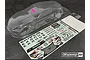 Clear, unpainted Bittydesign Ekanus 1/10 scale RC drag car body shell with a decal sheet and small hardware bag on a dark textured surface.