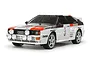A 1/10 scale Tamiya Audi Quattro A2 RC car model, featuring a white, brown, and red rally livery with number 3 on the side, isolated on a white background.