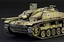 A painted and weathered scale model of a German StuG III tank on a dark background.