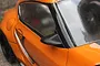 A close-up view of a black aero side mirror mounted on an orange RC car body shell.